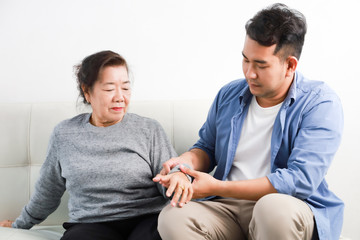 Asian senior woman mother and young man son in blue shirt massage his mother in living room