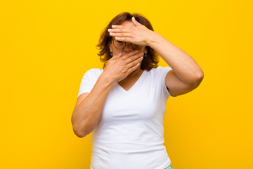 middle age woman covering face with both hands saying no to the camera! refusing pictures or...