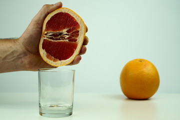 man squeezing half of juicy grapefruit to empty glass on white background, close up