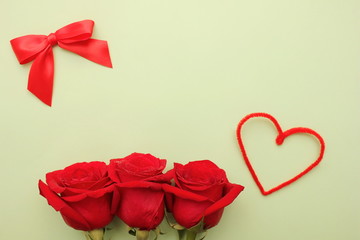 Three red roses with water drops on them . Red bow and heart next to them. Happy birthday card. Valentines day concept.