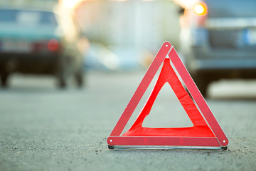 Red emergency triangle stop sign and broken car on a city street.