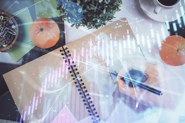 Forex chart hologram on hand taking notes background. Concept of analysis. Double exposure