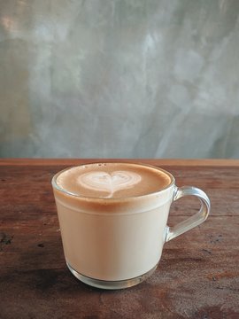 cup of hot latte coffee with heart shape art on wooden table