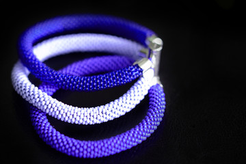 Fototapeta premium Beaded bracelet of three crocheted ropes on a dark background close up