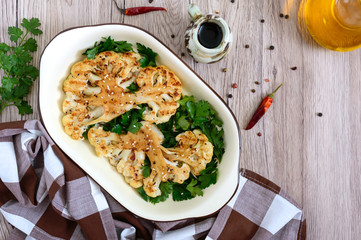 Baked cauliflower with greens on a wooden table. A beautiful cut of cauliflower. Healthy eating concept. The top view.