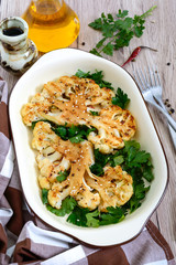 Baked cauliflower with greens on a wooden table. A beautiful cut of cauliflower. Healthy eating concept