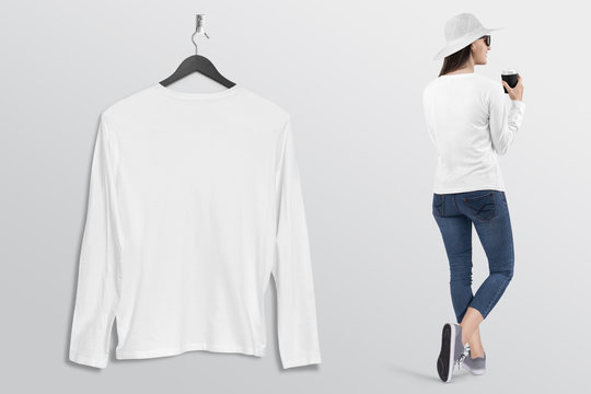 Hanging plain white long sleeve shirt on wall. Beside standing beautiful female model in blue denim jeans pant. 