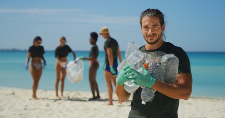 Portrait of an young male volunteer is smiling in camera satisfied with picking up a plastic litter...
