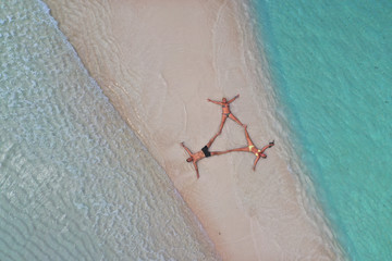 Aerial view of group of friends lying in the water in a triangle form on the beach of a desert island. 