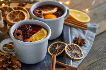 Christmas mulled wine in two rustic mugs with fruits and spices on wooden background