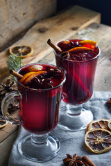hot mulled wine in two glasses with fruits and spices on wooden background