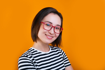 satisfied brunette young woman with happy expression, wears red glasses and casual t-shirt on yellow background