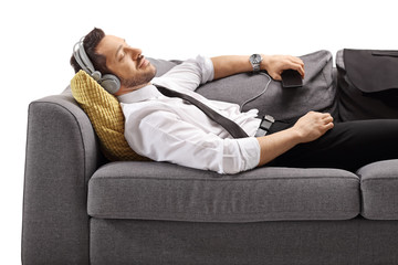 Young man in formal wear listening to music and lying on a couch