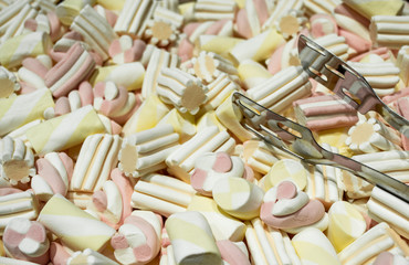 Close up of Marshmallows - white with yellow and pink colors in the form of spirals, flowers and stripes. Marshmallow candy tongs. Selling by weight