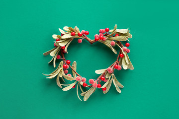 Green paper flat lay with decorative mistletoe with frosted leaves and red berries
