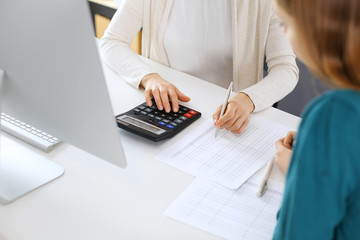 Accountant checking financial statement or counting by calculator income for tax form, hands close-up. Business woman sitting and working with colleague at the desk in office. Audit concept