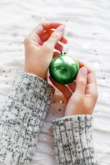 Woman holds New year decoration - sparkling neo mint colored ball for Christmas tree. White fabric...