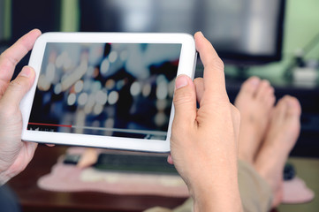 Cropped image of man hand holding tablet and watching video while sitting in livingroom.