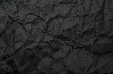 Texture of black crumpled paper. Dark paper background with chaotic bends. A sheet of black wrinkled paper