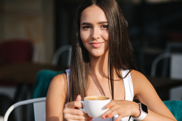 Close up of girl drinking cappuccino in the cafe. Beautiful brunette