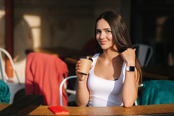 Attractive girl dring coffee on the terrace of the cafe from a craft cup. Beautiful brunette