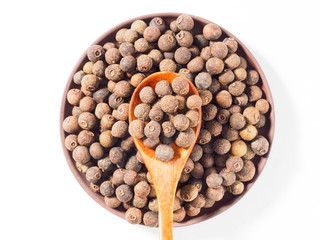 Allspice (Jamaica pepper) in clay plate and wooden spoon on white background