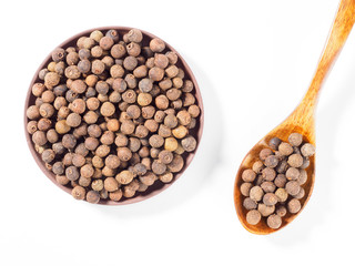 Allspice (Jamaica pepper) in the clay plate and wooden spoon diagonally on white background