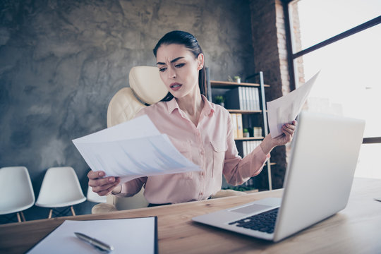 Low below angle view photo of entrepreneur sad upset unhappy comparing accounting paper of two periods sitting before laptop on desktop frowing with misunderstanding