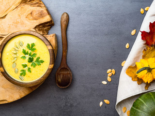hot yellow pumpkin and lentils soup, with seeds, parsley in oak wooden bowl, spoon from wood, decorative autumn foliage on kitchen linen towel, healthy food concept