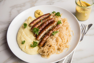 Kleine Bayrische Nürnberger Rostbratwürste mit Sauerkraut, Kartoffelpüree und Senf auf Marmor Tisch Hintergrund