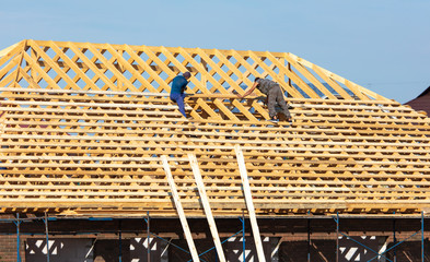 Workers are building the roof of the house from wood