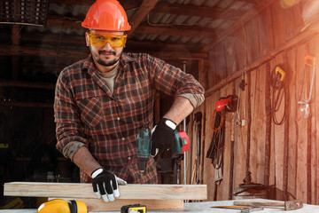 A man carpenter twists a screw into a tree with an electric screwdriver, male hands with a...