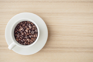 fresh roasted coffee beans in white cup on wood table, top view