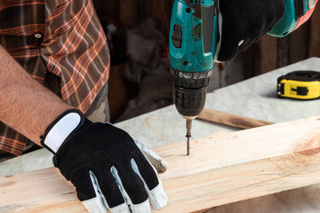 A man carpenter twists a screw into a tree with an electric screwdriver, male hands with a...