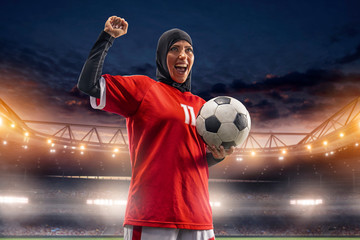Female muslim soccer player in hijab standing with a ball on a professional stadium © Alex