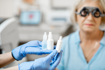 Nurse in medical gloves holding white bottles or droppers with eye medicine with senior patient on the background, close-up