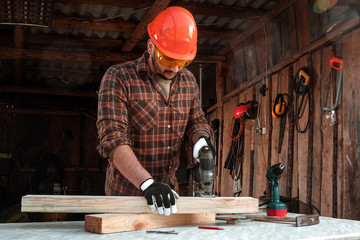 A man carpenter cuts a wooden beam using an electric jigsaw, male hands with an electric jigsaw...