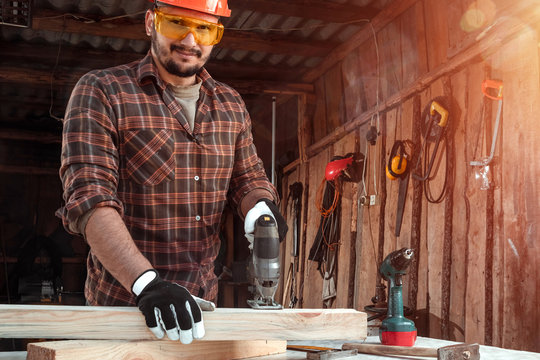 A man carpenter cuts a wooden beam using an electric jigsaw, male hands with an electric jigsaw closeup. Work with wood.