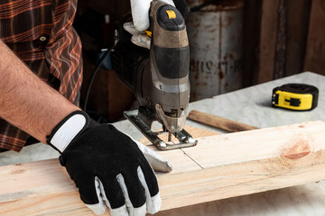 A man carpenter cuts a wooden beam using an electric jigsaw, male hands with an electric jigsaw closeup. Work with wood.