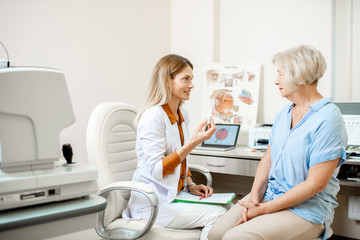 Senior woman patient talking with female ophthalmologist during a medical consultation at the ophthalmologic office. Doctor offering eye medcine for a patient - obrazy, fototapety, plakaty