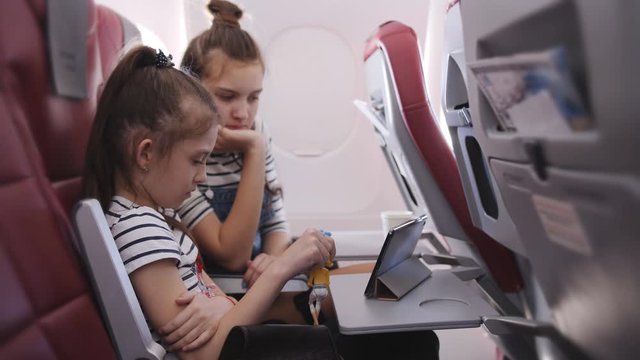 Two sisters in the cabin during the flight watching cartoons on the tablet.