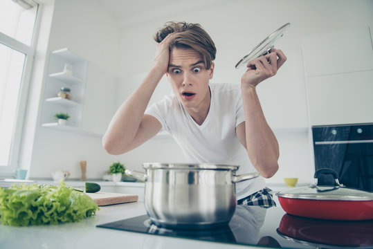 Close-up portrait of his he nice attractive overwhelmed clueless puzzled guy making dinner lunch looking at boiling bouillon at light white modern style interior house indoors