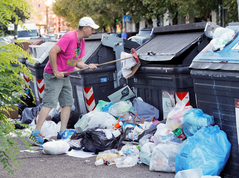 A resident tries to open a rubbish bin using a broom in Rome