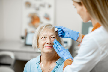 Female doctor dripping eye drops on eyes of a senior patient during a treatment at the...
