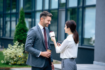 journalist holding microphone and talking with businessman in formal wear