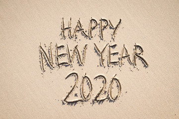 Happy New Year 2020 message handwritten in raised textured letters on a sand beach with smooth copy space