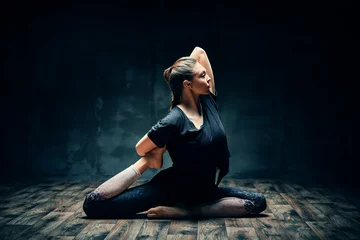 Draagtas Jonge vrouw die yoga beoefent in een pose met een koningsduif op één been in een donkere kamer © GVS