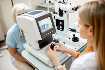 Ophthalmologist examining eyes of a senior patient using digital microscope during a medical examination in the ophthalmologic office - obrazy, fototapety, plakaty