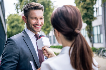 journalist holding microphone and talking with businessman in formal wear