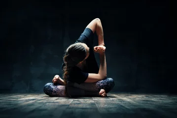 Fototapeten Young woman doing yoga Padmasana pose variation on dark room © GVS
